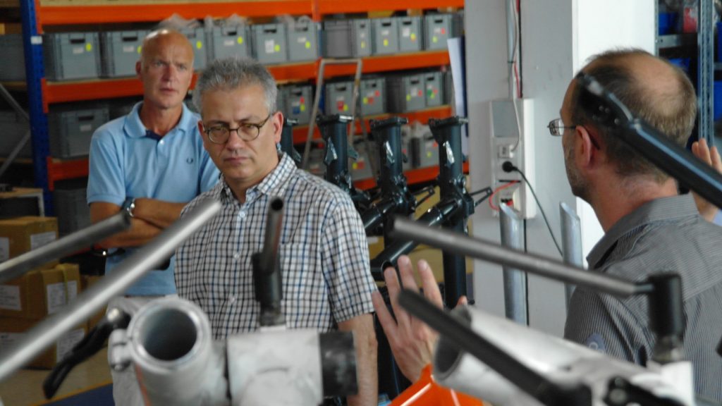 Paul Hollants (vorne rechts) erläutert Tarek Al-Wazir (Mitte) den Bau von Liegedreirädern.