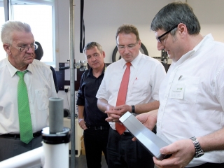 In der Werkstatt der Manufaktur erläutert Gobax-Geschäftsführer Robert Dorn (ganz rechts)dem Ministerpräsidenten (ganz links) den neu entwickelten Hochleistungs-Akkupack mit modernster Lithium-Ionen-Mangan-Technologie.